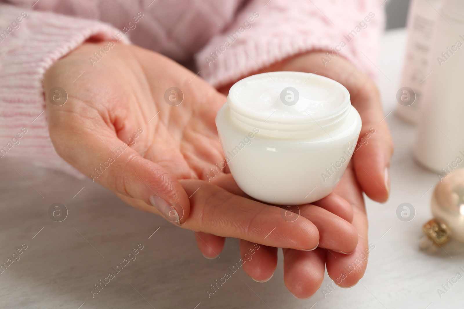 Photo of Woman holding jar of cream at light table, closeup. Cosmetic product for winter