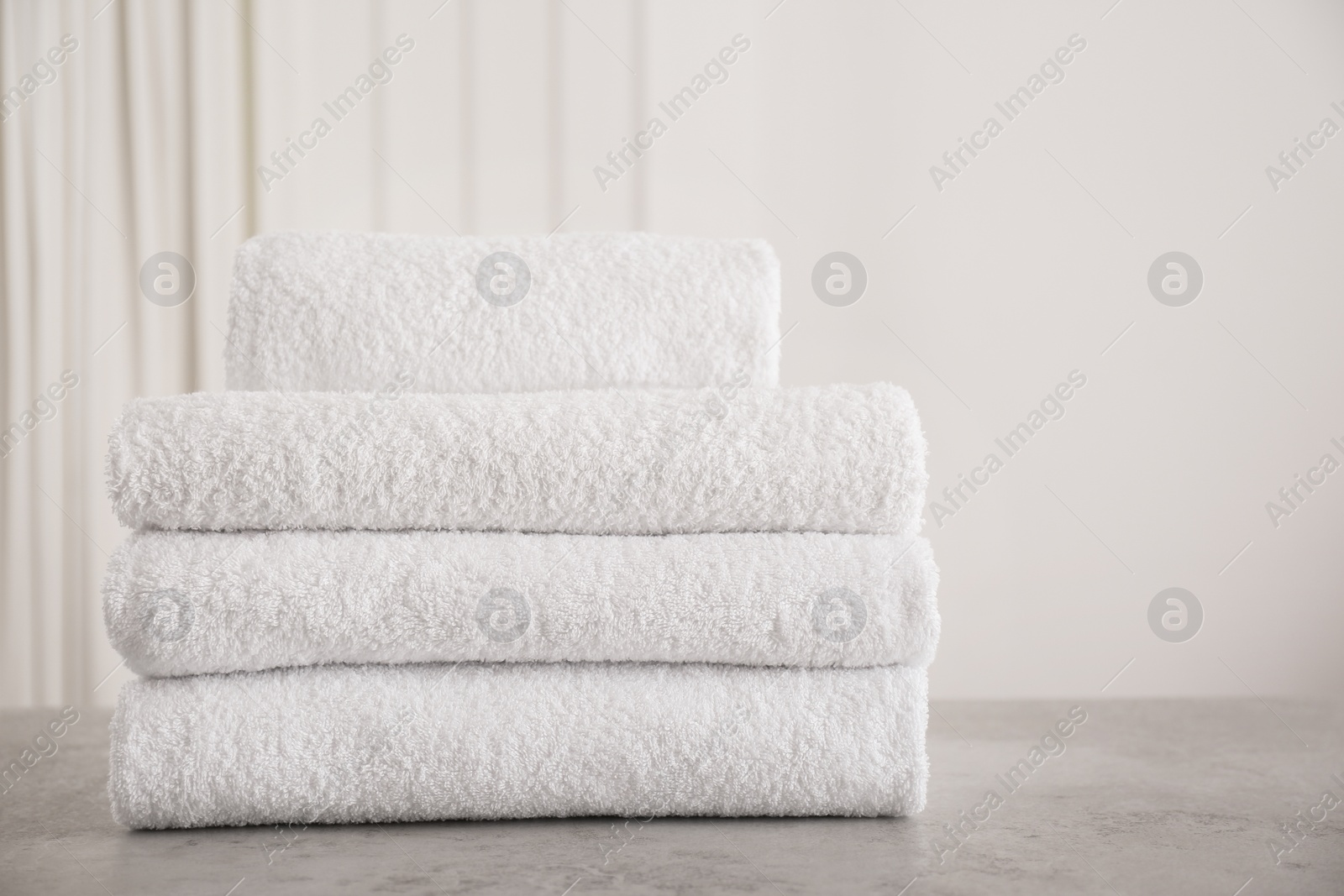 Photo of Stack of fresh towels on light grey stone table in bathroom