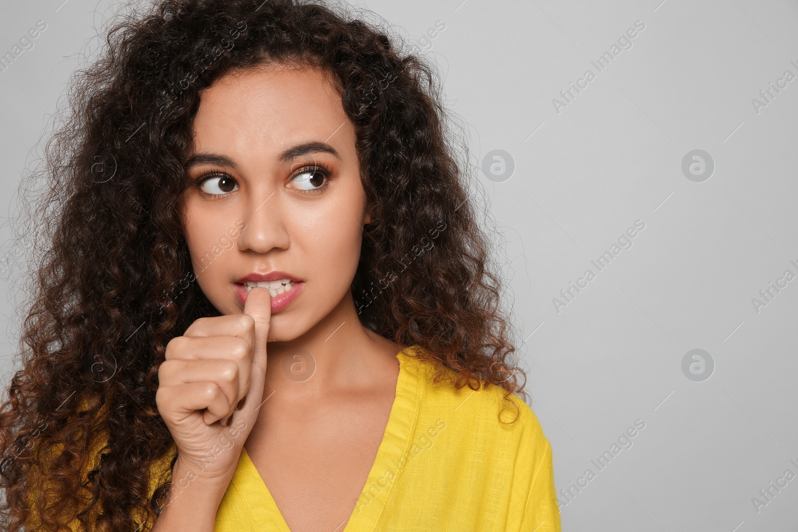 Photo of African-American woman biting her nails on grey background. Space for text