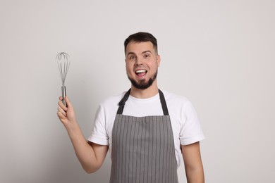 Photo of Excited professional confectioner in apron holding whisk on light grey background