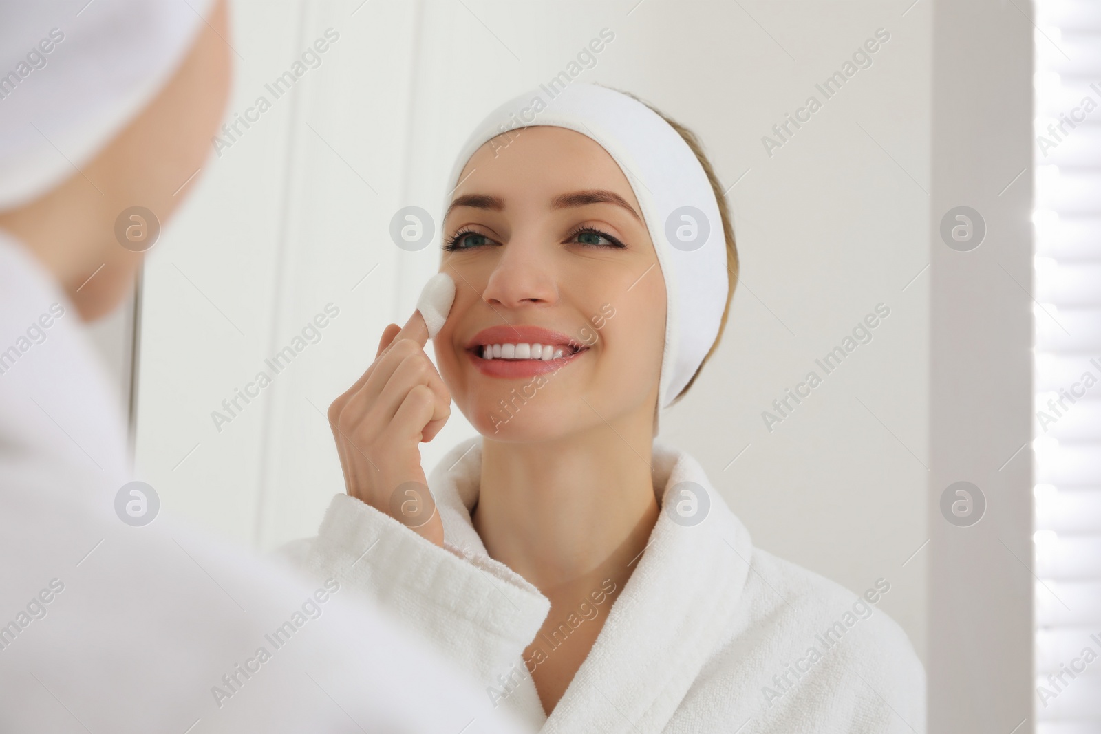 Photo of Woman using silkworm cocoon in skin care routine near mirror at home