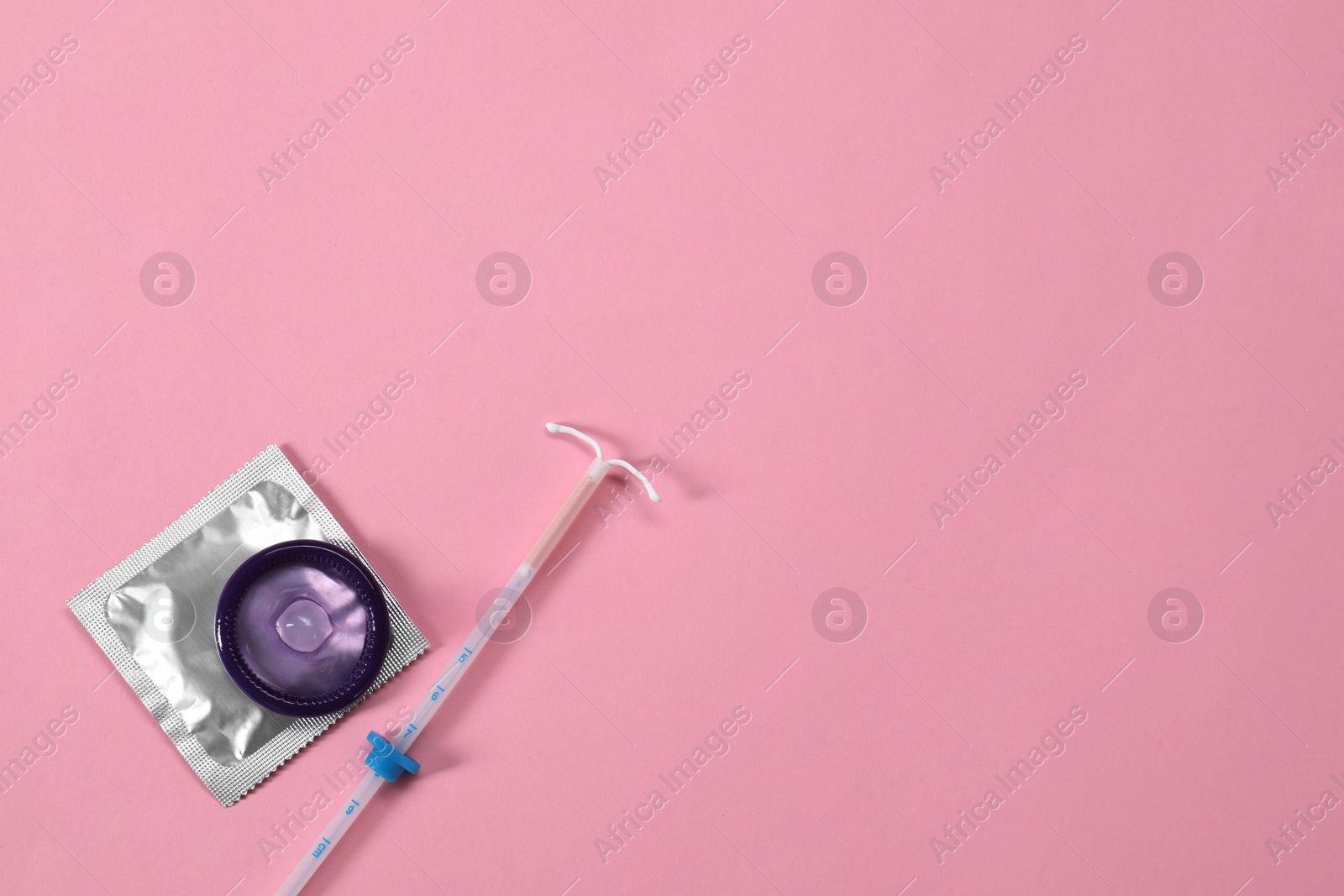 Photo of Contraception choice. Condoms and intrauterine device on pink background, flat lay. Space for text