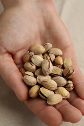 Woman holding tasty roasted pistachio nuts at table, closeup