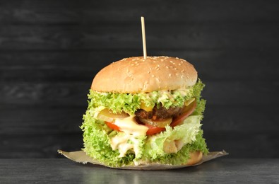 Photo of Burger with delicious patty on gray table against dark background
