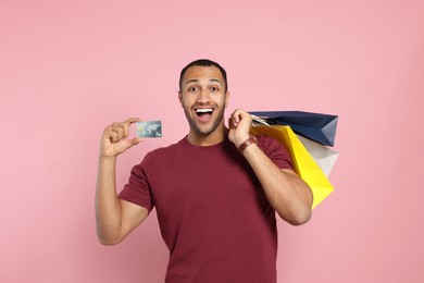 Photo of Happy African American man with shopping bags and credit card on pink background