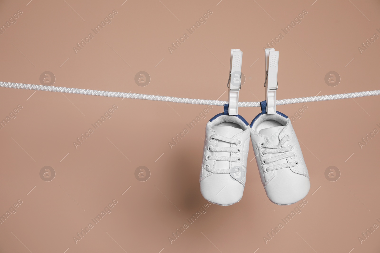 Photo of Cute small baby shoes hanging on washing line against brown background, space for text