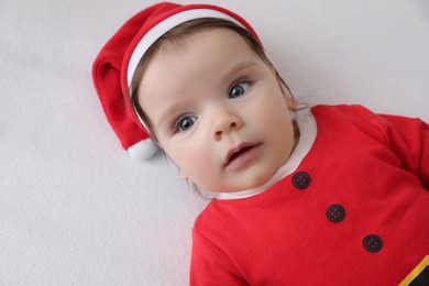 Photo of Cute baby wearing festive Christmas costume on white bedsheet, top view