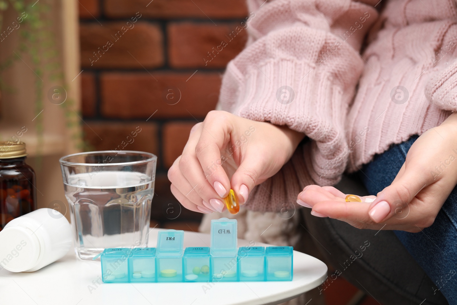 Photo of Woman taking pill from plastic container at white table indoors, closeup