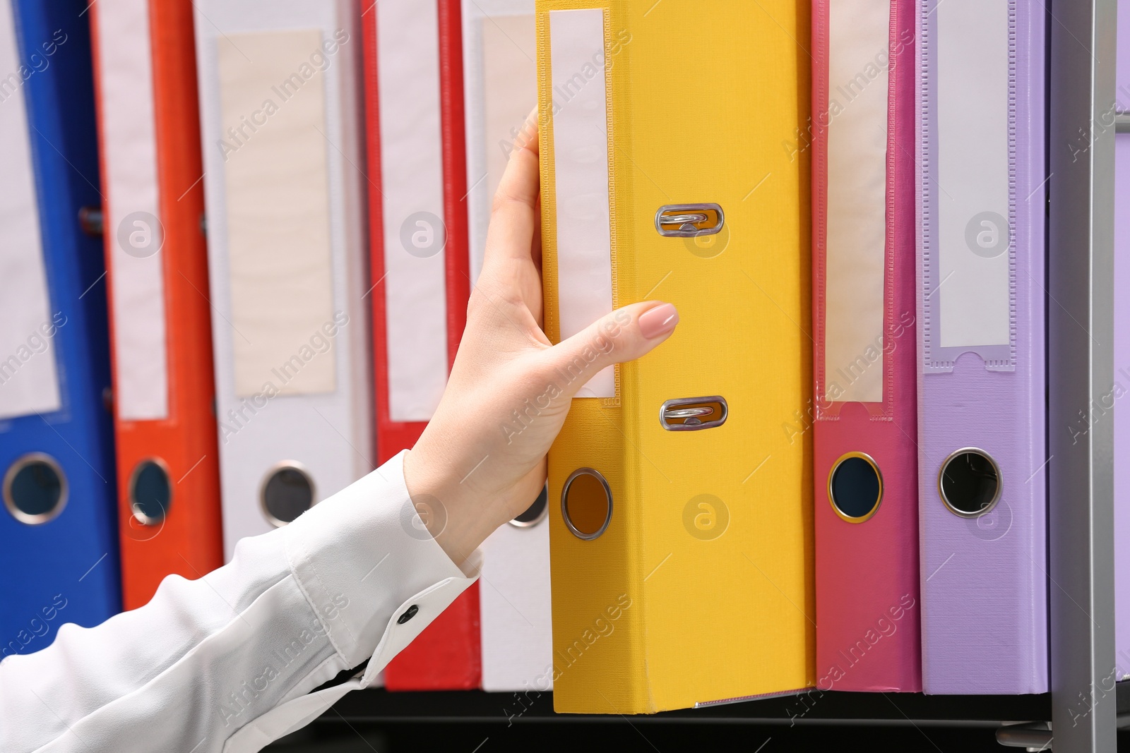 Photo of Woman taking folder with documents from shelf in office, closeup