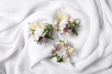 Photo of Stylish boutonnieres on white silk, flat lay