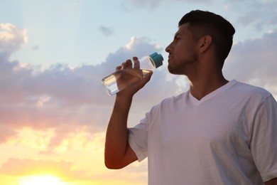 Photo of Man drinking water to prevent heat stroke outdoors at sunset, space for text