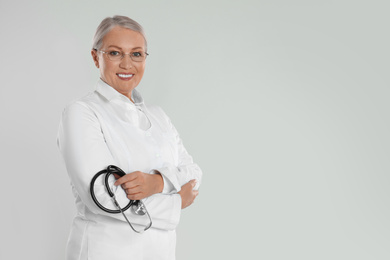 Portrait of mature doctor with stethoscope on light grey background. Space for text