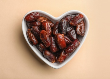 Heart shaped bowl with sweet dried date fruits on color background, top view