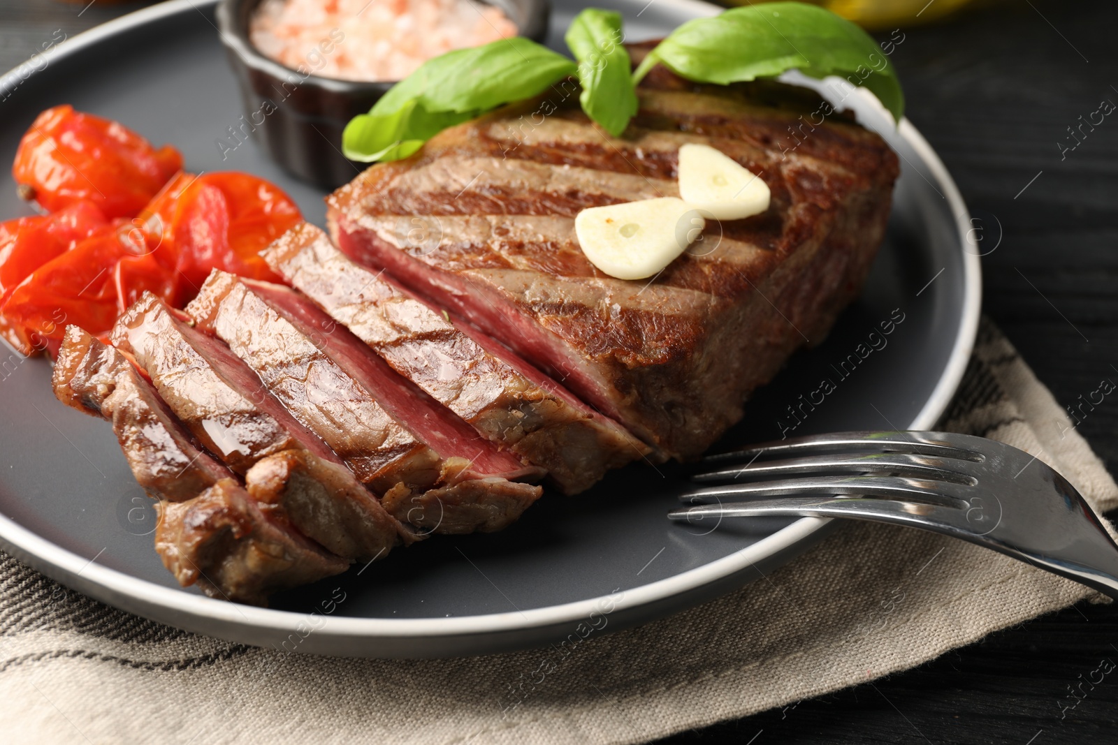 Photo of Delicious grilled beef steak served with spices and tomatoes on table, closeup
