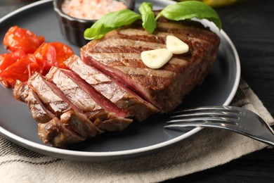 Delicious grilled beef steak served with spices and tomatoes on table, closeup