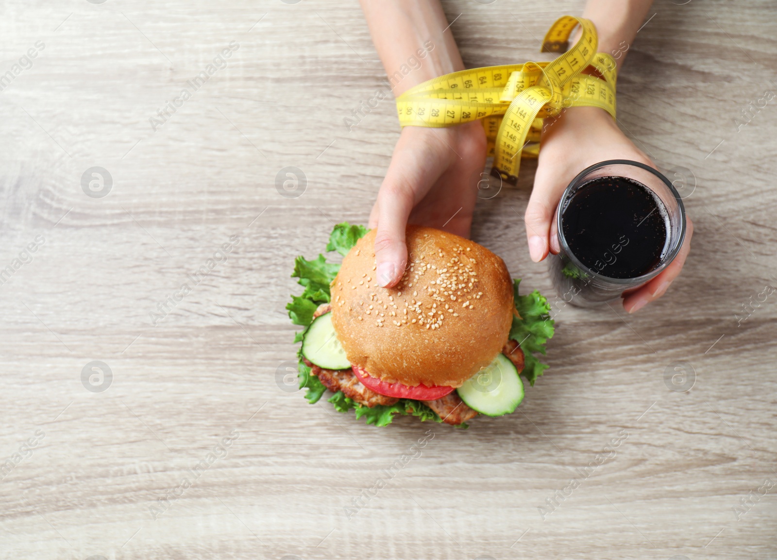 Photo of Woman with tied hands holding tasty sandwich and glass of cold drink at wooden table, top view. Healthy diet