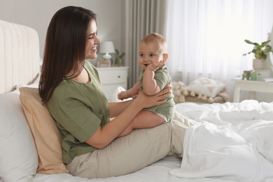 Happy young mother with her cute baby on bed at home