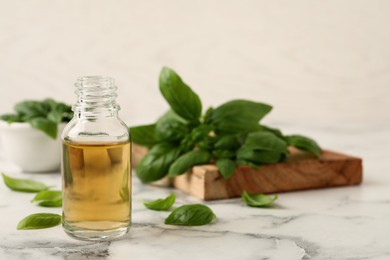 Photo of Glass bottle of basil essential oil and leaves on white marble table. Space for text