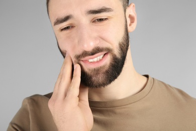 Young man suffering from toothache on light background