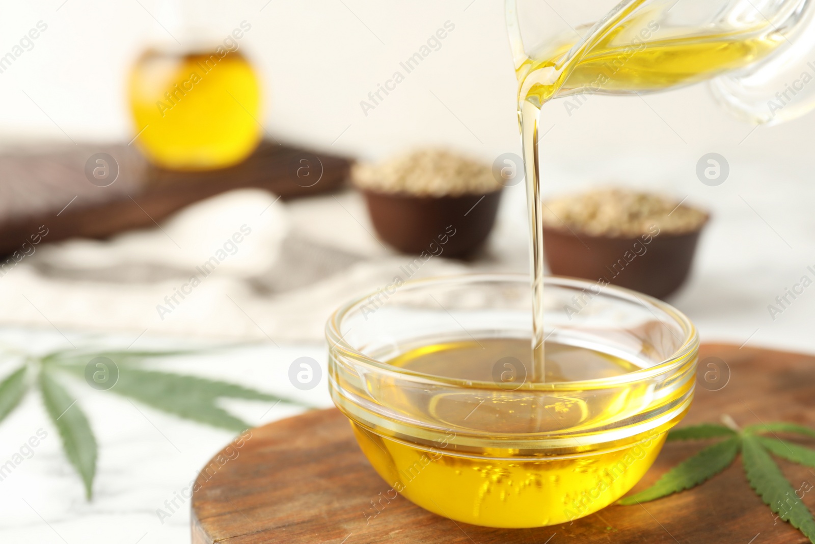 Photo of Hemp oil pouring from sauce boat into bowl on table