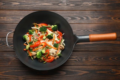 Stir fried noodles with mushrooms and vegetables in wok on wooden table, top view