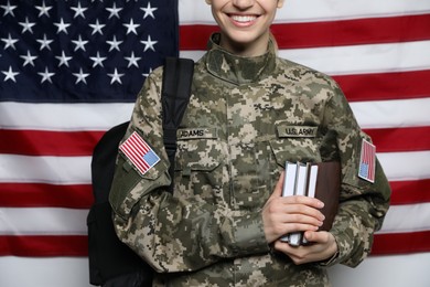 Photo of Female cadet with backpack and books against American flag, closeup. Military education