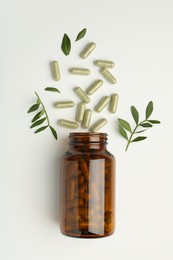 Bottle, vitamin capsules and leaves on white background, flat lay