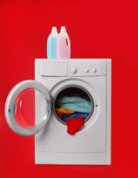Photo of Modern washing machine with laundry and detergents on red background