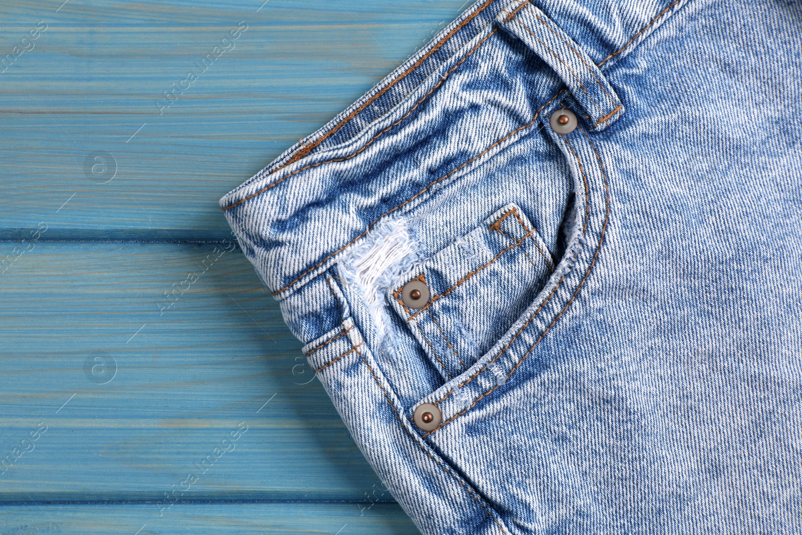 Photo of Stylish light blue jeans on wooden background, closeup of inset pocket