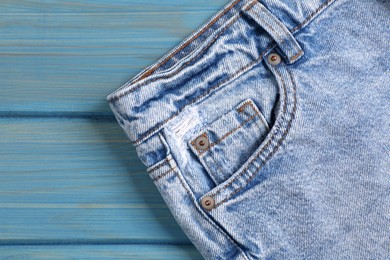 Stylish light blue jeans on wooden background, closeup of inset pocket