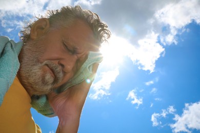Photo of Senior man with towel suffering from heat stroke outdoors, low angle view. Space for text