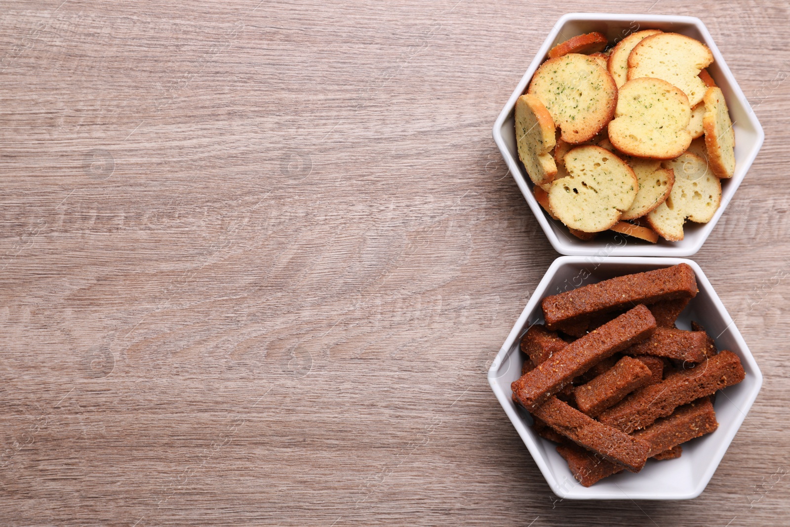 Photo of Different crispy rusks in bowls on wooden table, flat lay. Space for text