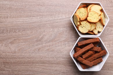 Different crispy rusks in bowls on wooden table, flat lay. Space for text