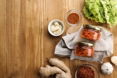 Photo of Delicious kimchi with Chinese cabbage and ingredients on wooden table, flat lay. Space for text