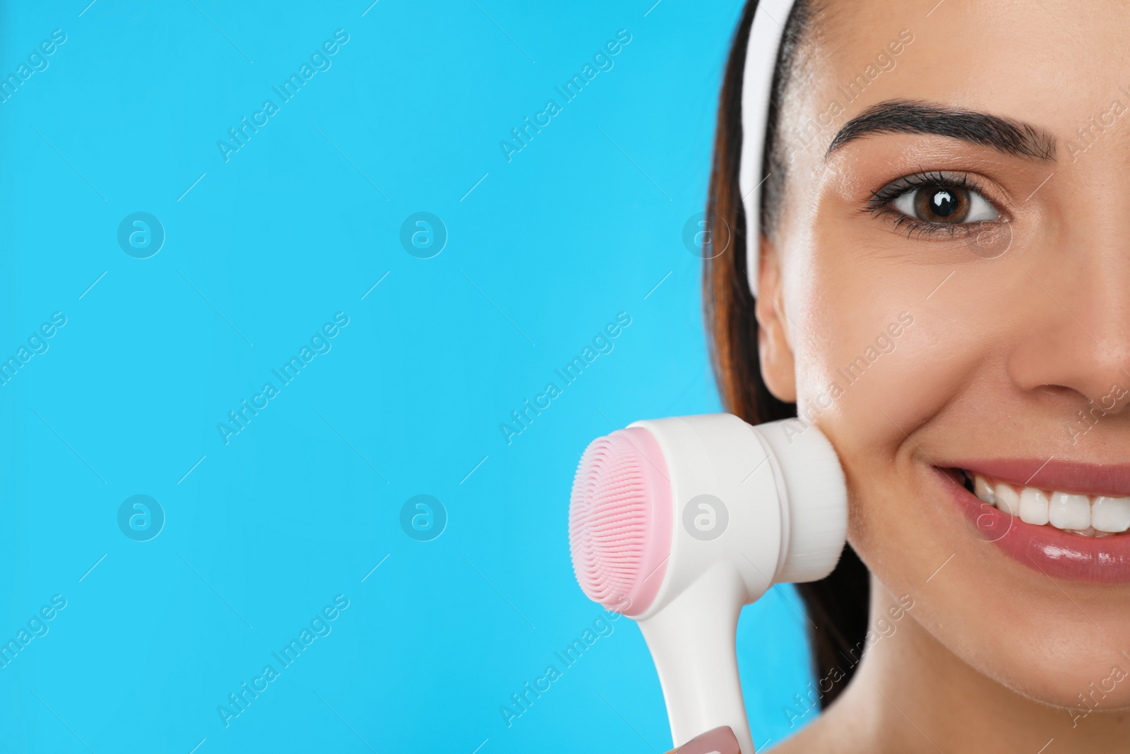 Photo of Young woman using facial cleansing brush on light blue background, closeup with space for text. Washing accessory