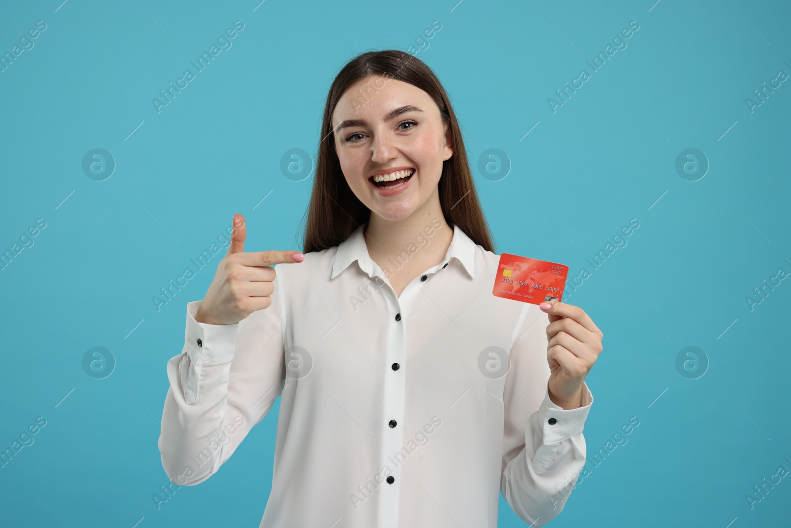 Photo of Happy woman pointing at credit card on light blue background