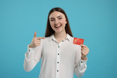 Happy woman pointing at credit card on light blue background