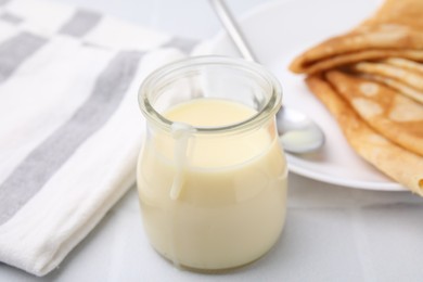 Photo of Tasty condensed milk in jar and crepes on white table, closeup