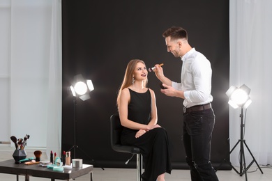 Photo of Professional makeup artist working with beautiful young woman in photo studio