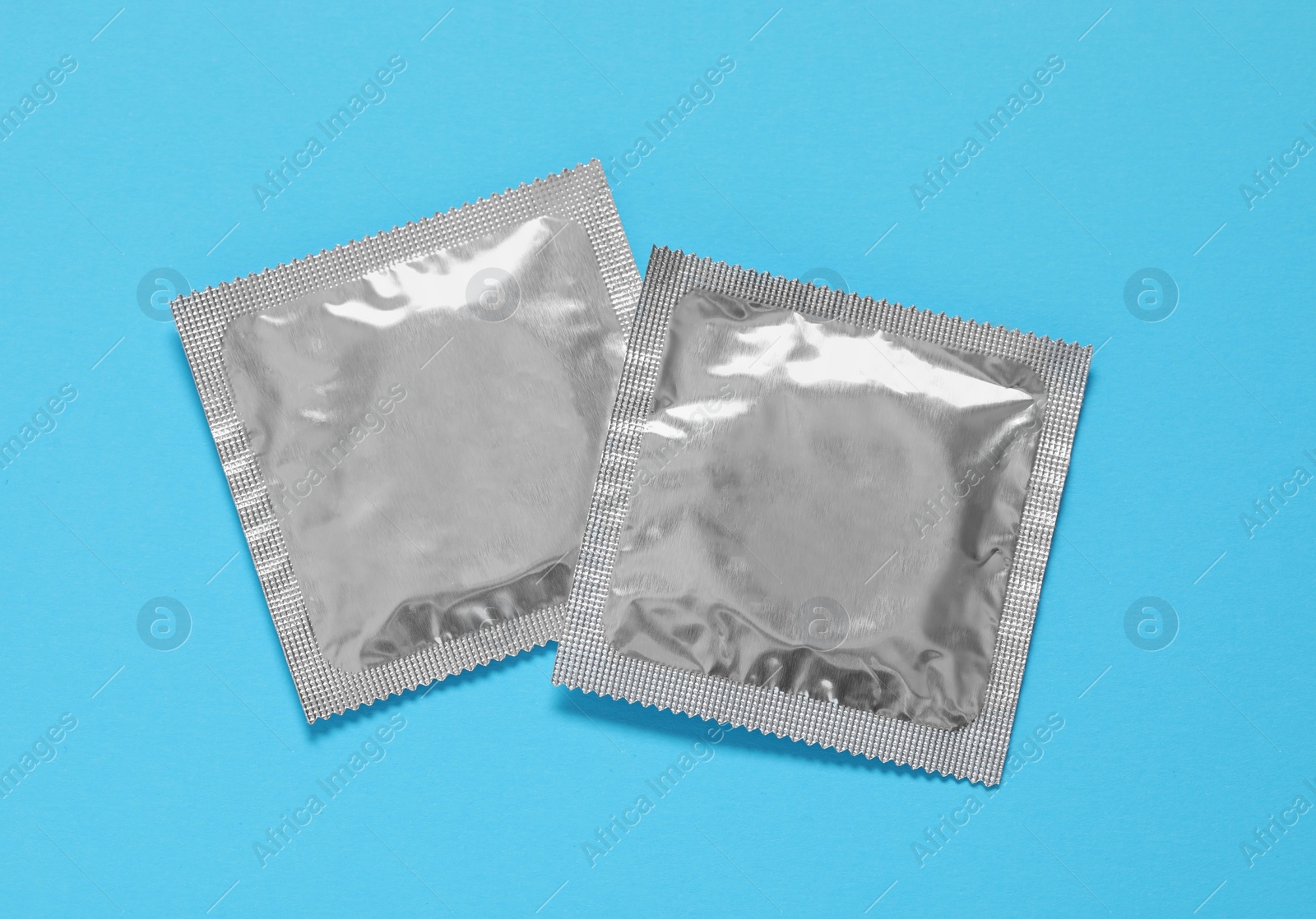 Photo of Condom packages on light blue background, flat lay. Safe sex