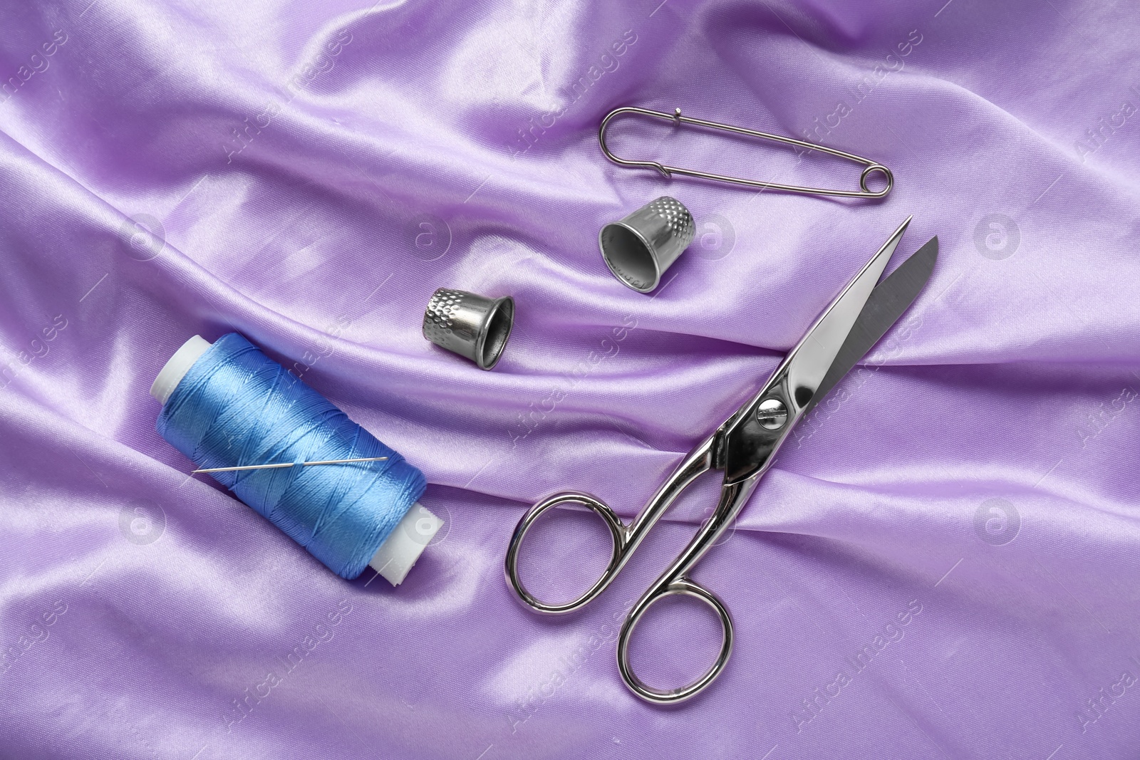 Photo of Silver thimbles and other sewing accessories on purple cloth, flat lay