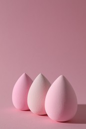 Three colorful makeup sponges on pink background