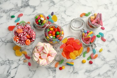 Jars with different delicious candies on white marble table, flat lay