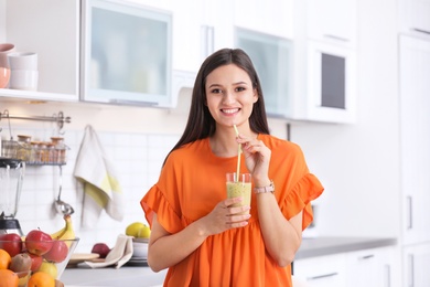 Young woman with glass of tasty healthy smoothie in kitchen