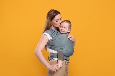 Mother holding her child in baby wrap on orange background