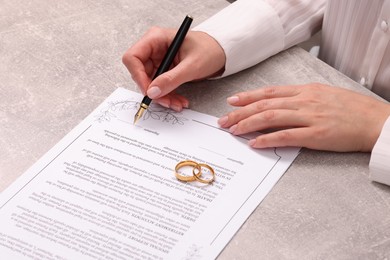Woman signing marriage contract at light grey table, closeup