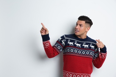 Man in Christmas sweater pointing on white background, space for text