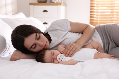 Photo of Young mother resting near her sleeping baby on bed at home