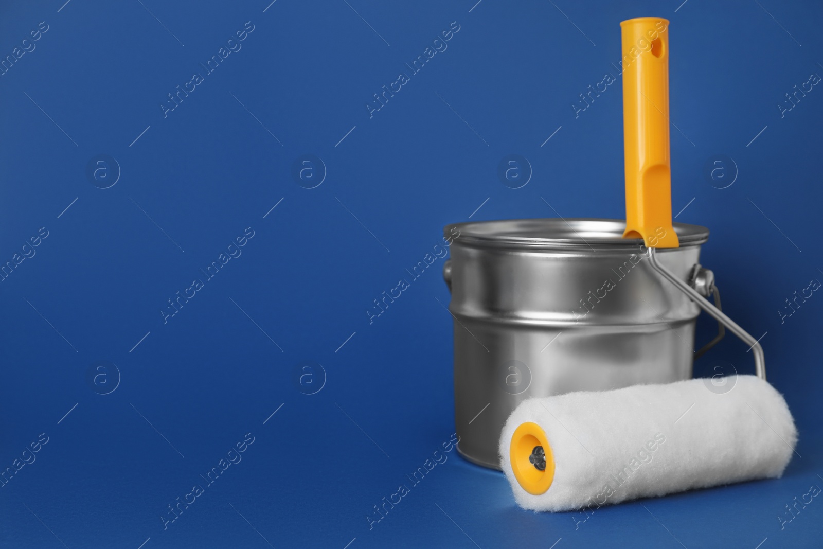 Photo of Can of paint and roller brush on blue background. Space for text
