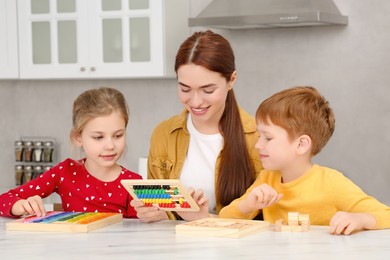 Photo of Happy mother and children playing with different math game kits at white marble table in kitchen. Study mathematics with pleasure
